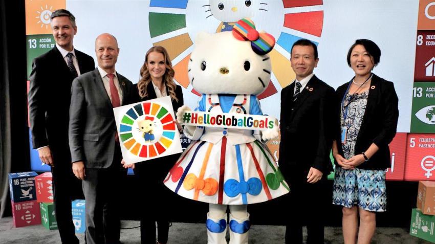 SDGsの背景とHelloGlobalGoalsのパネルを囲むハローキティと関係者。2019年の国連公式記事掲載写真。